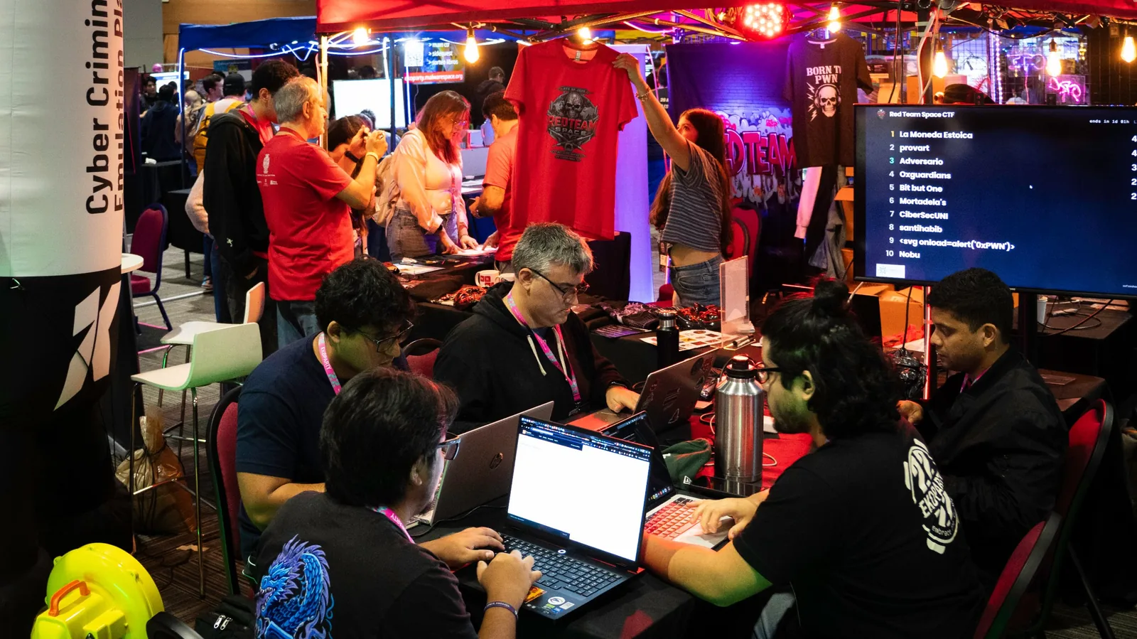 Participantes concentrados en sus laptops durante la competencia CTF con el ranking en pantalla