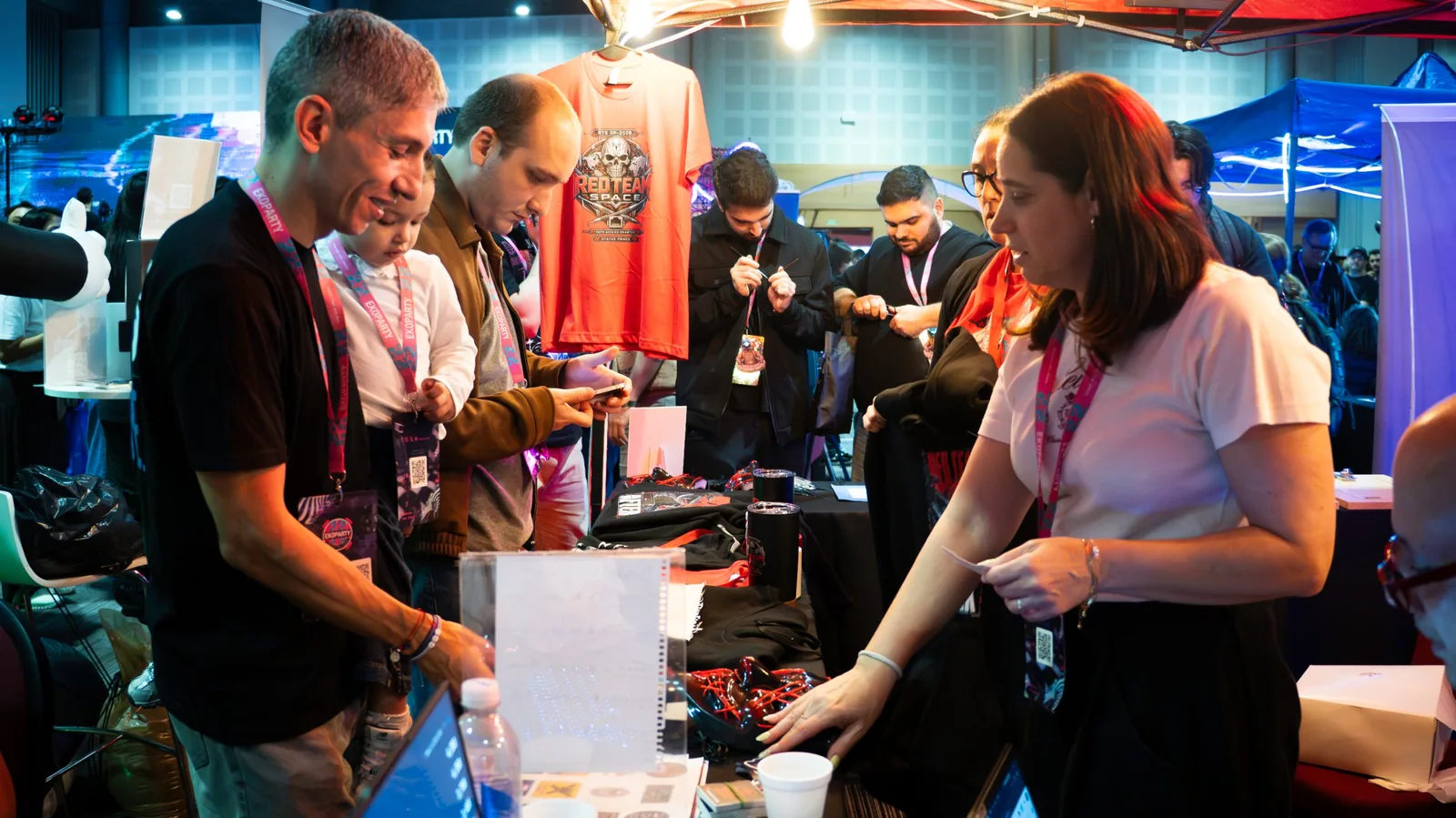 Asistentes con credenciales de Ekoparty en la mesa de merchandising del Red Team Space