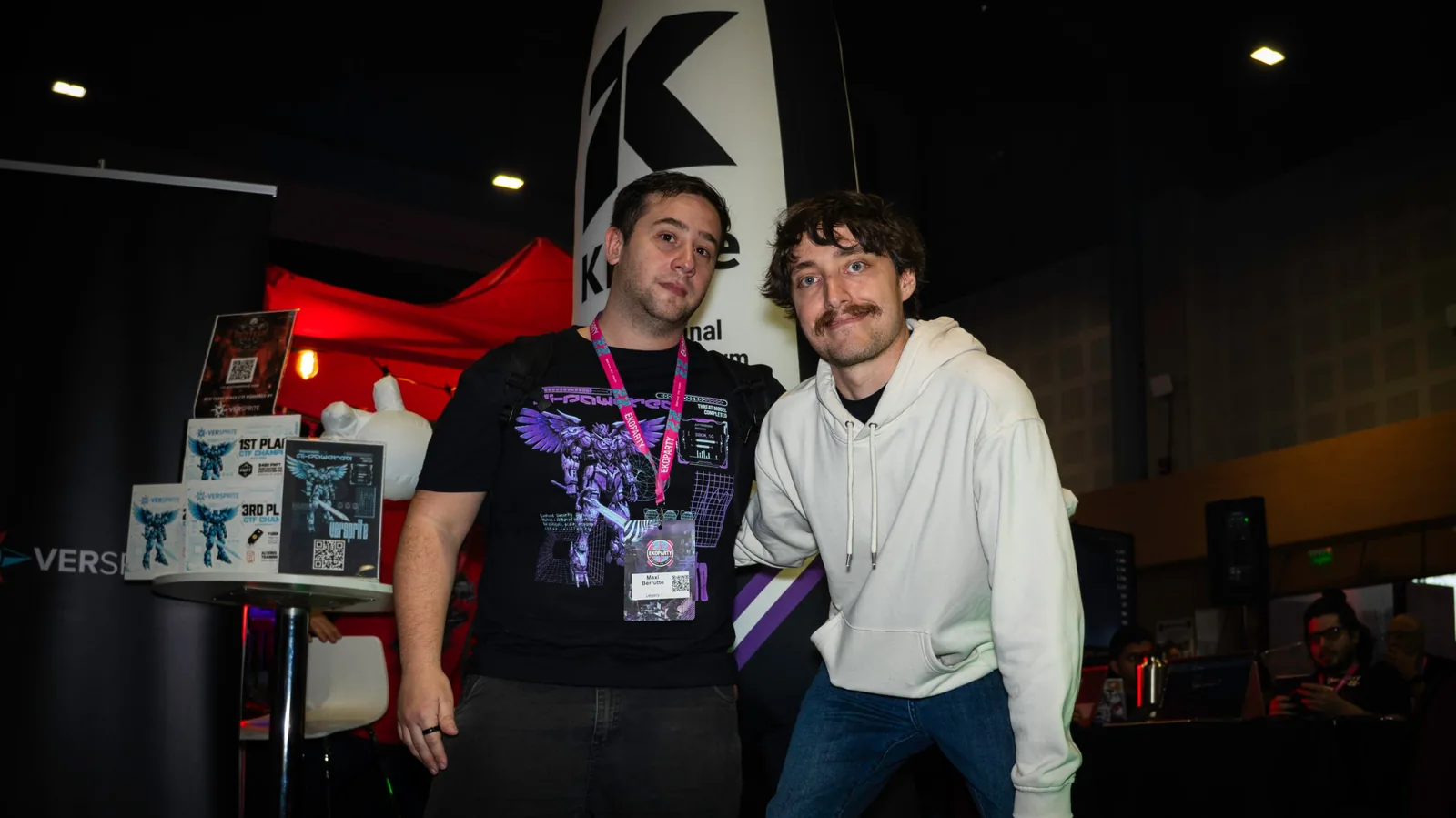 Dos asistentes posando frente al stand con la credencial de Ekoparty