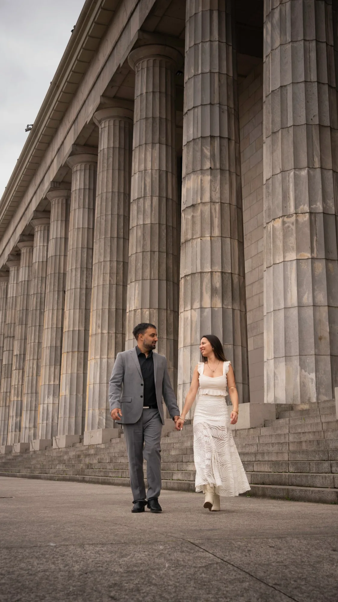 Marcelo y Noelia caminando de la mano frente a las columnas de la Facultad de Derecho