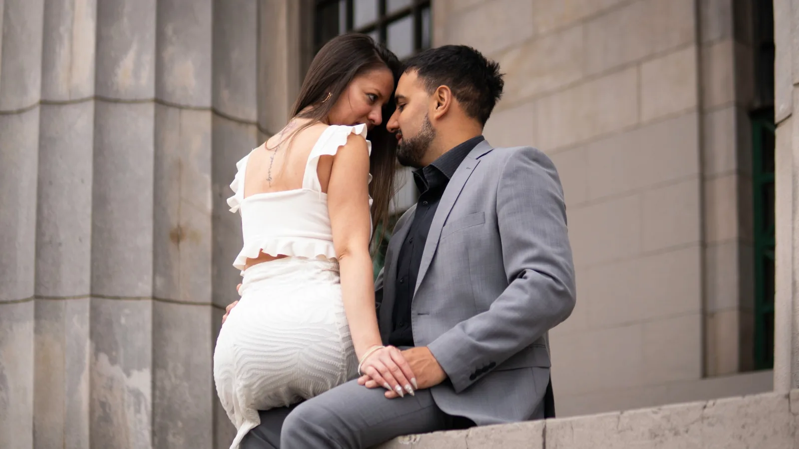 Pareja sentada junto a una columna, frente con frente, en una sesión de novios